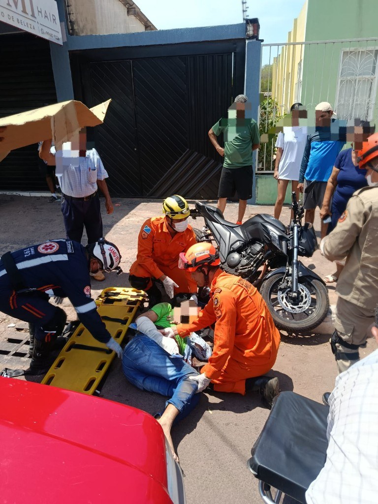 Bombeiros militares imobilizam o motociclista de 45 anos no asfalto, com prancha rígida ao lado, enquanto moradores acompanham o atendimento