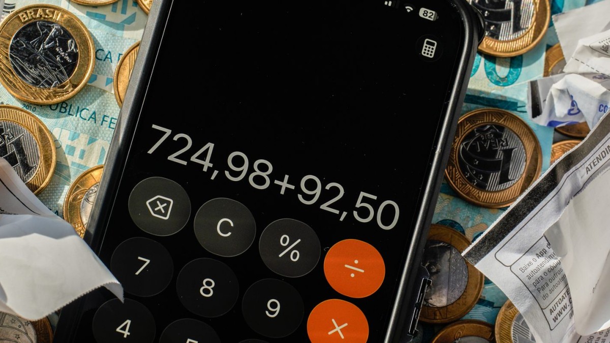 Celular com calculadora sobre moedas, cédulas e comprovantes — orçamento familiar